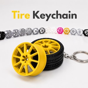 Puede incluir: Una colección de llaveros de neumático con el texto Tire Keychain arriba. Los llaveros cuentan con un neumático de goma negro y una llanta amarilla de múltiples radios unida a una anilla de metal plateado. Se ven otras llantas de colores.