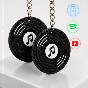 Op de afbeelding: Twee zwarte ronde sleutelhangers in de vorm van vinylplaten met een witte muzieknoot in het midden. Elke sleutelhanger heeft een zilveren metalen ketting en ring. De tekst 3DKEYLABS PRINTED WITH PRECISION staat in de linkerbovenhoek.
