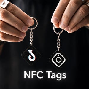 Può includere: Due tag NFC quadrati neri attaccati a portachiavi in metallo argentato. Un tag presenta il logo TikTok bianco e rosso, mentre l'altro mostra l'icona della fotocamera Instagram bianca. Il testo NFC Tags è stampato in bianco nella parte inferiore.