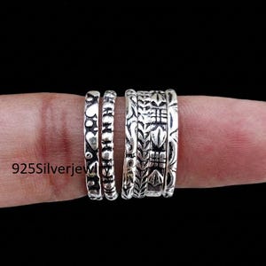 Puede incluir: Un conjunto de cinco anillos de plata esterlina con varios patrones en relieve, incluyendo corazones, formas geométricas y motivos botánicos. Los anillos están hechos de plata 925 y presentan un acabado pulido con detalles oscuros.