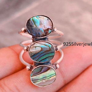 May include: A sterling silver ring featuring three stacked oval abalone shell inlays with iridescent blue, green, and purple hues. The band is composed of three thin silver wires that connect to the settings. The text 925Silverjewlry is visible.