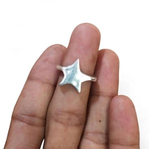 May include: A silver-toned ring featuring a prominent four-pointed star design. The star has smooth, rounded edges and a polished metallic surface that reflects light. The band of the ring is thin and connects to the centre of the star shape.