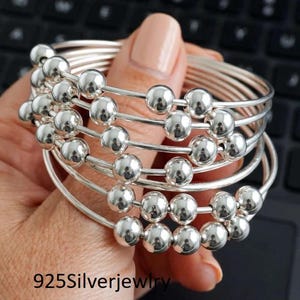 May include: A multi-strand silver bangle bracelet featuring numerous polished, reflective silver-tone beads strung along thin, circular wire bands. The text 925Silverjewlry is visible in the lower left corner of the image, indicating the material composition.