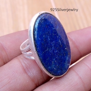 May include: A silver ring featuring a large, oval-shaped, deep blue lapis lazuli gemstone with visible gold-colored flecks. The band consists of three thin, parallel silver wires. The text 925Silverjewelry is visible in the upper right corner.
