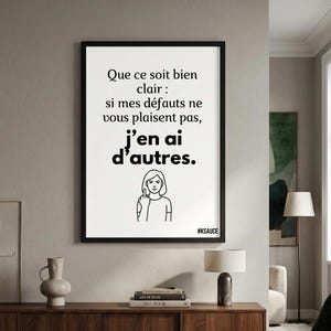 May include: A framed print with French text, including the phrase "Que ce soit bien clair". The print features a drawing of a person giving the middle finger. The print is displayed on a wall above a wooden cabinet.