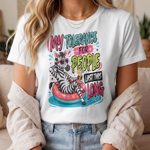 Peut inclure: Un t-shirt blanc avec un motif de zèbre portant des lunettes de soleil roses, se relaxant dans une bouée colorée avec une boisson. Le texte indique : MY TOLERANCE FOR PEOPLE LAST THIS LONG. Le design inclut de l'eau bleue et des étoiles roses.
