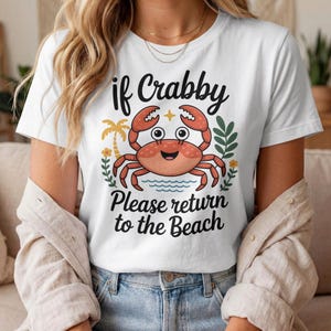 Peut inclure: T-shirt blanc avec un motif de crabe souriant et le texte "if Crabby Please return to the Beach". Le crabe est orange avec des yeux noirs et des pinces rouges. Le motif comprend un palmier et des éléments floraux.
