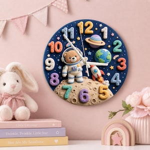 Può includere: Un orologio da parete per bambini con un orsetto astronauta su una superficie lunare. Il quadrante blu navy presenta numeri colorati, pianeti e un razzo. Circondato da un tema decorativo rosa e bianco.