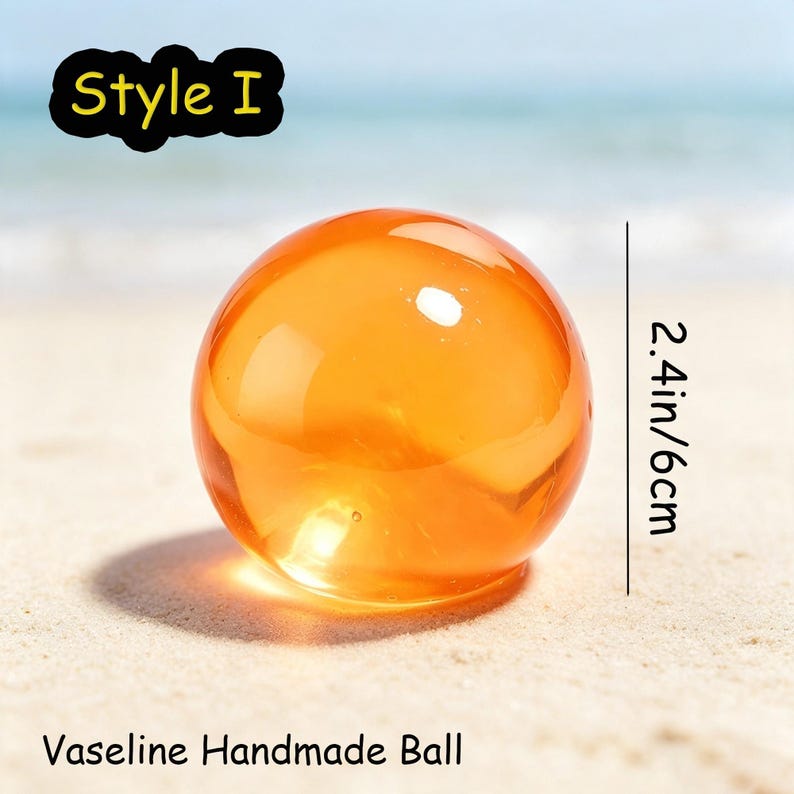 May include: A translucent orange spherical object labeled Style I and Vaseline Handmade Ball. The sphere has a diameter of 2.4 inches. The object is smooth and round, reflecting light on its surface while casting a shadow on the ground below.
