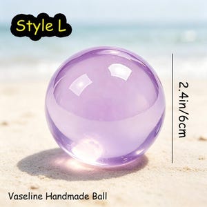May include: A smooth, translucent purple sphere labeled Style L and Vaseline Handmade Ball. The object is shown with a vertical line indicating a diameter of 2.4 inches. The sphere has a glossy finish and reflects light on its curved surface.