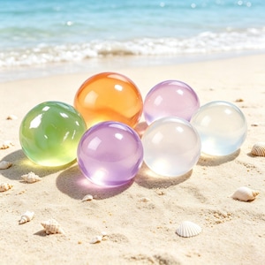 May include: A collection of six smooth, translucent, spherical orbs in various colors including orange, light green, purple, lavender, and clear. The spheres are arranged in a cluster, each reflecting light on its polished, glossy surface.