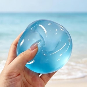 Può includere: Un oggetto rotondo, liscio e traslucido di colore azzurro con una finitura lucida. La superficie riflette la luce, creando brillanti riflessi bianchi sulla sua forma curva simile a un globo. L'oggetto ha un aspetto morbido e flessibile.