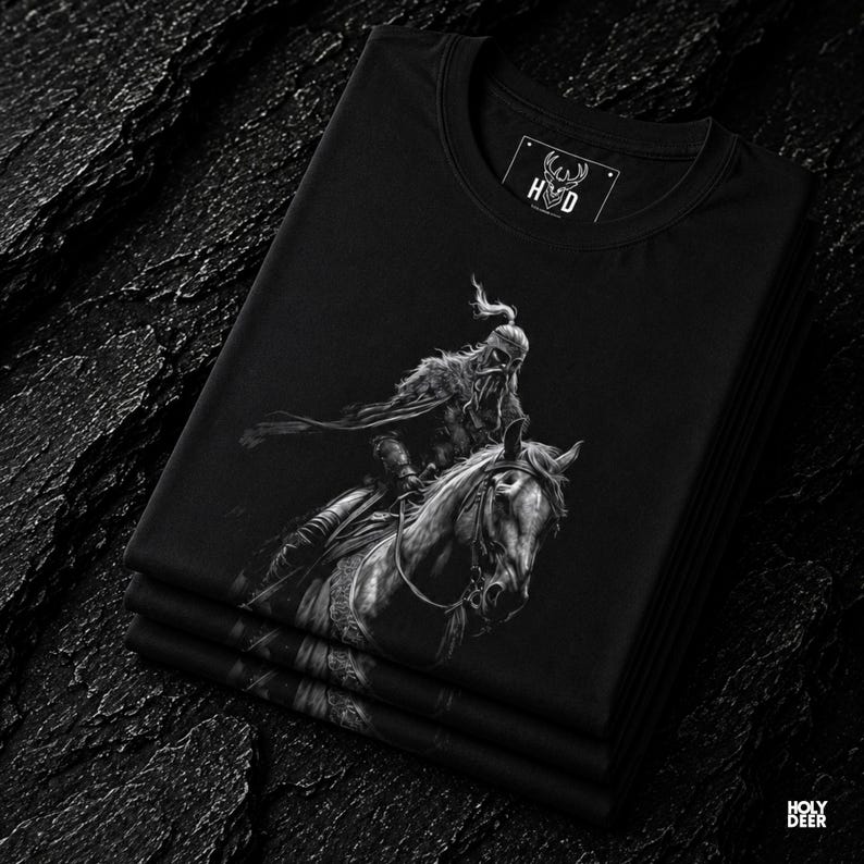 Close up detail of the deep design style graphic print on a soft black fabric fold, showcasing the fine white reflections on the iron helmet, the realistic horse mane texture, and the fluid armor lines. Lifestyle photograph of the Turkish warrior tee stacked neatly within a premium clothing collection to highlight the solid black cotton tone and the high-contrast white fantasy line art. This piece serves as an absolute masterpiece.