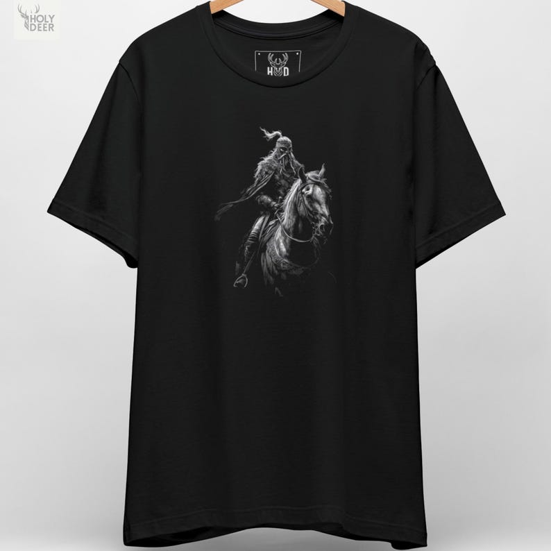 A premium Turkish warrior tee folded neatly on a dark textured rock background, showcasing a highly detailed monochrome illustration of a nomad cavalryman on his horse, centered on the chest. This Attila the Hun shirt captures pure steppe rider apparel energy.