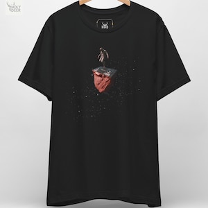 Op de afbeelding: Zwart t-shirt met een grafische print. Het ontwerp toont een figuur op een DJ-mixer bovenop een rode rots, tegen een donkere achtergrond met witte spikkels. Het shirt heeft een ronde hals en korte mouwen.