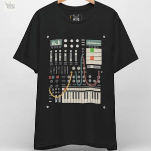 May include: Black t-shirt featuring a detailed graphic of a synthesizer control panel with knobs, sliders, and a keyboard. The design includes colorful wires and the text "H D" and "HOLY DEER" in the upper left corner.