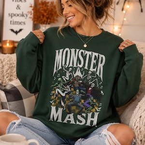 Op de afbeelding: Een donkergroene sweater met ronde hals en een grafische print van diverse klassieke monsters die op een geblokte vloer dansen. De tekst "MONSTER MASH" staat in grote witte letters boven en onder de kleurrijke illustratie van de wezens.