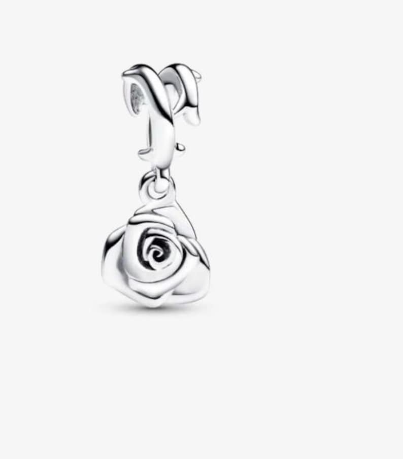 May include: A polished silver charm featuring a dangling rose pendant. The charm has a curved, smooth bail at the top designed for attachment to a bracelet or necklace chain, with a detailed, layered rose flower shape hanging below it.