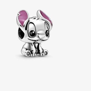 May include: A silver charm bead shaped like the character Stitch, featuring large black eyes, a small nose, and prominent ears with pink enamel detailing on the inner sections. The character is depicted in a seated position with visible paws.