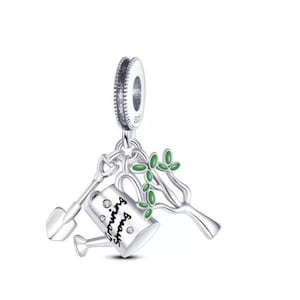 Könnte beinhalten: Ein silberner Charm mit einer Schaufel, einer Gießkanne mit der Aufschrift Growing Strong und kleinen klaren Steinen sowie einem Baumzweig mit grünen Emaille-Blättern. Der Charm hat eine kreisförmige Öse mit strukturiertem Rand und dem Stempel S925.