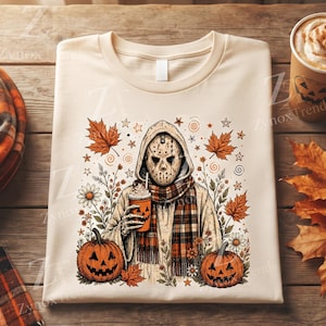 May include: A beige t-shirt featuring a graphic of a hockey-masked figure in a hooded sweatshirt and plaid scarf, holding a pumpkin-faced cup. The design includes orange maple leaves, daisies, and two jack-o'-lanterns at the base of the figure.
