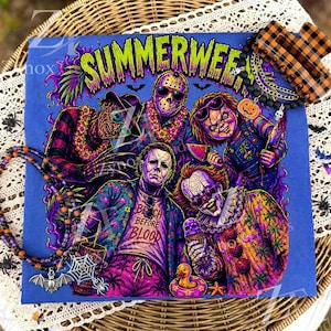May include: A blue t-shirt featuring a graphic print titled SUMMERWEEN with horror movie characters wearing tropical attire. The design includes a beaded necklace with a bat charm and a plaid hair claw clip resting on the fabric.