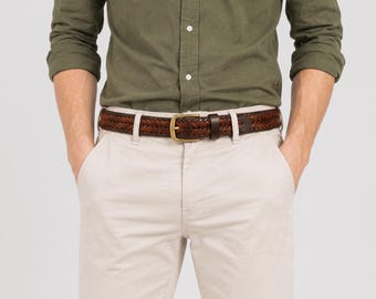 Peut inclure: Une ceinture tressée en cuir marron foncé avec une boucle en métal doré, portée avec une chemise à manches longues vert olive et un pantalon beige clair. La ceinture présente une texture tressée et un fermoir à ardillon unique.