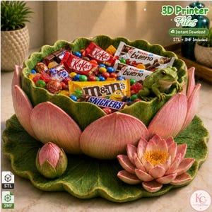 Peut inclure: Un bol décoratif en forme de fleur de lotus épanouie avec des feuilles vertes et des pétales roses, rempli de chocolats assortis. Une petite figurine de grenouille verte est posée sur le bord intérieur du bol, reposant sur un grand nénuphar.
