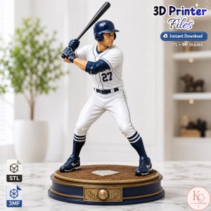 Puede incluir: Una figura impresa en 3D de un jugador de béisbol con uniforme blanco y detalles azul marino, que lleva un casco y sostiene un bate negro. El jugador tiene el número 27 en el pecho y se apoya en una base circular con un emblema de béisbol. El texto dice 3D Printer Files, Instant Download, STL + 3MF Included.