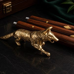 May include: A polished gold-toned metal fox figurine with intricate textured fur detailing, positioned in front of three dark brown wooden walking stick segments featuring small brass inlays and threaded metal connectors at the ends.