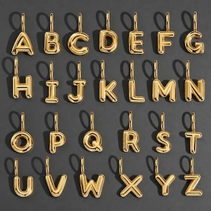 Könnte beinhalten: Eine Sammlung von sechsundzwanzig einzelnen Buchstabenanhängern aus goldfarbenem Metall, angeordnet in alphabetischer Reihenfolge von A bis Z. Jeder Buchstabe hat ein glattes, abgerundetes, dreidimensionales ballonartiges Design mit einer kleinen Öse.