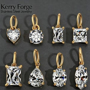 Peut inclure: Huit pendentifs en métal doré avec des pierres de zircone cubique transparentes et facettées de formes variées : cœur, rond, rectangulaire, carré, poire, ovale et marquise. Chaque pendentif a un anneau doré. Le texte indique Kerry Forge Stainless Steel Jewelry.