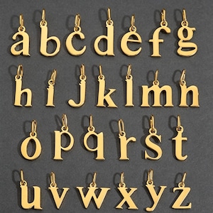 May include: A collection of twenty-six individual gold-toned metal letter charms, each featuring a small jump ring at the top. The set includes the complete lowercase alphabet from a to z, arranged in four rows against a dark grey background.