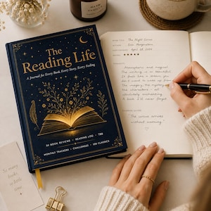 Może przedstawiać: Granatowy dziennik zatytułowany "The Reading Life" ze złotymi akcentami, zapaloną świecą i filiżanką herbaty. Dziennik jest otwarty, a osoba w nim pisze. Mała karta głosi "So many books, so little time."