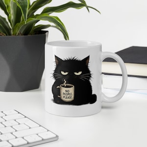 Peut inclure: Un mug en céramique blanche orné d'une illustration graphique d'un chat noir touffu à l'expression grincheuse. Le chat tient une tasse plus petite avec le texte NO PEOPLE. PLEASE. imprimé dessus. Le mug possède une anse standard et une finition lisse.