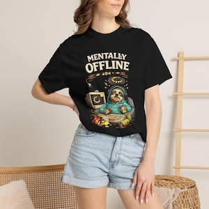 Peut inclure: T-shirt noir avec l'inscription "MENTALLY OFFLINE 404" au-dessus d'un paresseux de dessin animé portant un casque et assis devant un ordinateur. Le paresseux tient une boisson et est entouré de collations.