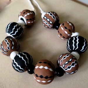 May include: A necklace made of brown, black and white ceramic beads with wavy and striped patterns.