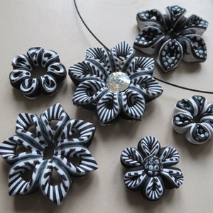 Puede incluir: Un conjunto de joyas de arcilla polimérica en blanco y negro con diseños de flores. Las flores tienen un patrón a rayas y algunas tienen un centro de pedrería. Las joyas incluyen un collar y pendientes.