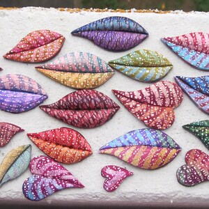 May include: A collection of 15 colorful, hand-painted ceramic hearts and lips. The hearts and lips are decorated with various patterns and colors, including pink, purple, blue, green, and red.