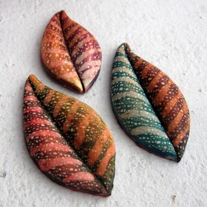May include: Three ceramic leaf-shaped pendants with different patterns. The first leaf is pink and brown with white speckles. The second leaf is green and brown with white speckles. The third leaf is orange and brown with white speckles.