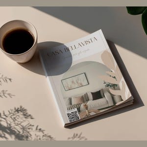 May include: A cup of coffee sits next to a magazine titled "CASA BELLAVISTA" with a QR code. The magazine features a photo of a living room. The scene is set on a beige surface with shadows and a plant.