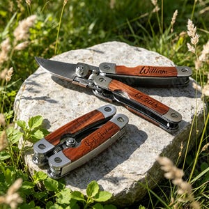 以下が含まれることがあります： 剪定刃を備えたシルバーと木製のハンドルを持つマルチツールで、ハンドルには「William」と「Est. 2015」の刻印があり、その横には木製のハンドル表面に「Best Gardener」と刻印された折りたたみ式のマルチツールが置かれています。