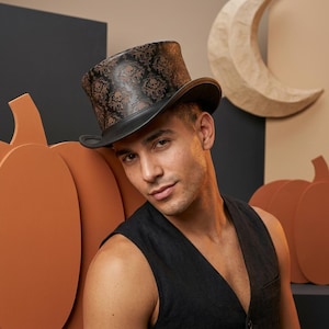 May include: A black top hat with a brown skull and floral pattern. The hat has a curved brim and a tall crown. The hat is part of a Halloween costume. The background includes orange pumpkin cutouts and a paper moon.
