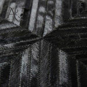 May include: A black and dark gray cowhide patch pillow cover featuring a geometric star pattern created with stitched seams. The surface has a textured hair-on-hide finish with a visible logo in the corner reading American Hide.