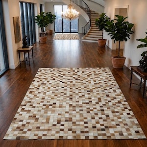 Può includere: Un tappeto rettangolare con un design patchwork composto da piccole tessere quadrate in varie tonalità di marrone, beige, crema e bianco. Il tappeto è steso su un pavimento in legno scuro e presenta un motivo a griglia ripetuto sulla superficie.