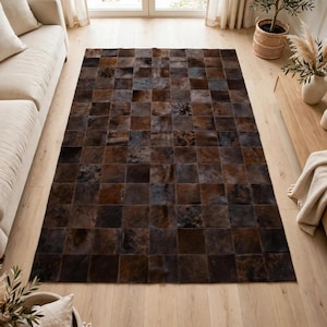 May include: A rectangular area rug composed of a grid of square patches in varying shades of dark brown, chocolate, and black. The rug features a patchwork design with natural hair-on-hide textures, creating a multi-tonal surface across the floor.