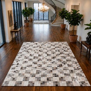 Puede incluir: Una alfombra rectangular con un patrón de mosaico de pequeñas baldosas cuadradas en varios tonos de blanco, gris y negro. La alfombra está colocada sobre un suelo de madera oscura en una habitación grande con ventanas altas y plantas.