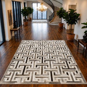 May include: A rectangular area rug featuring a repeating geometric Greek key pattern in shades of grey, black, and white. The rug is composed of individual panels arranged in a grid, creating a textured surface with a high-contrast interlocking design.