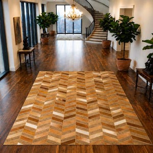 Puede incluir: Una alfombra rectangular con un patrón de espiga compuesto por parches de cuero cosidos en varios tonos de marrón, bronceado y crema. La alfombra está colocada sobre un suelo de madera oscura en una habitación grande con techos altos.