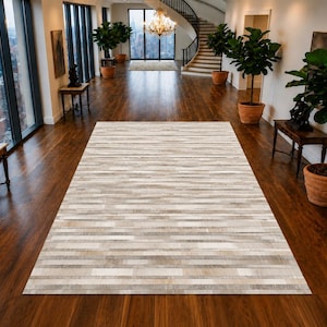 May include: A rectangular area rug featuring a horizontal striped pattern composed of varying shades of beige, cream, tan, and light grey. The rug has a flat, textured surface with a patchwork design of narrow, elongated rectangular strips.